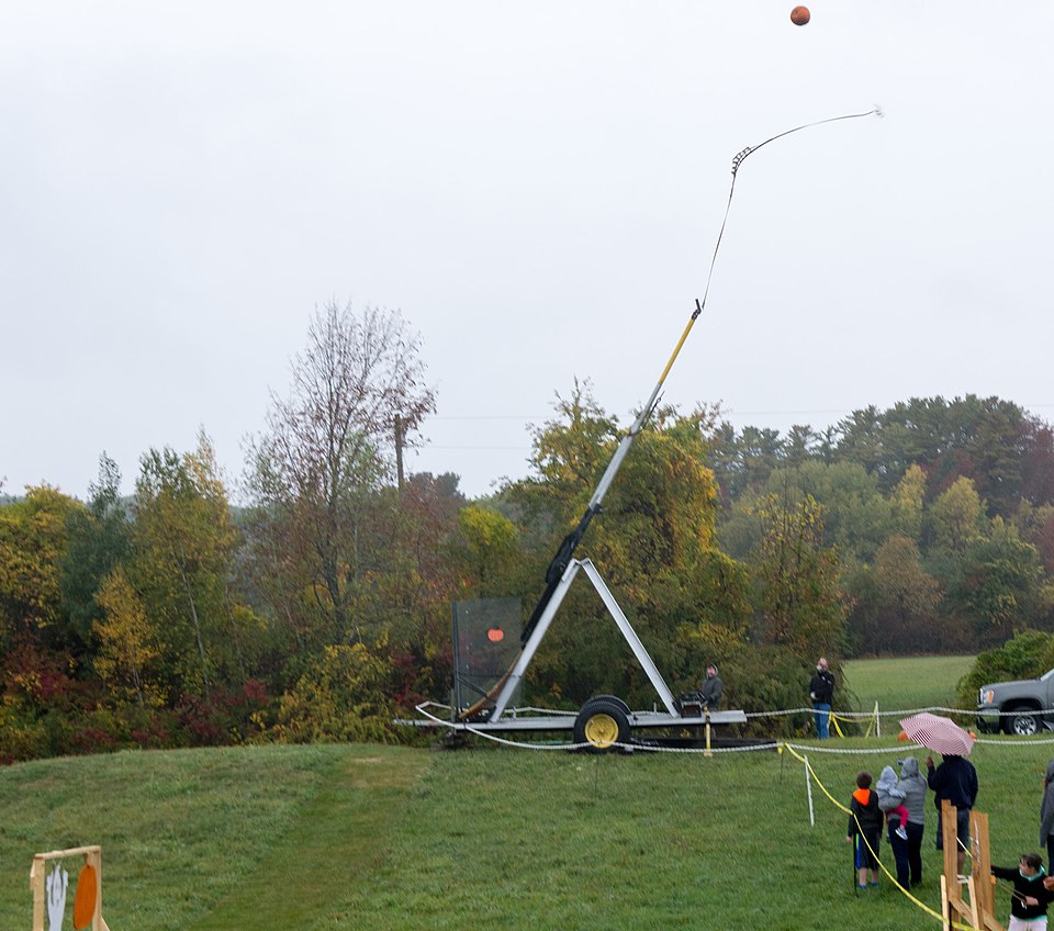 A trailer-mounted trebuchet launching a pumpkin at a fall festival